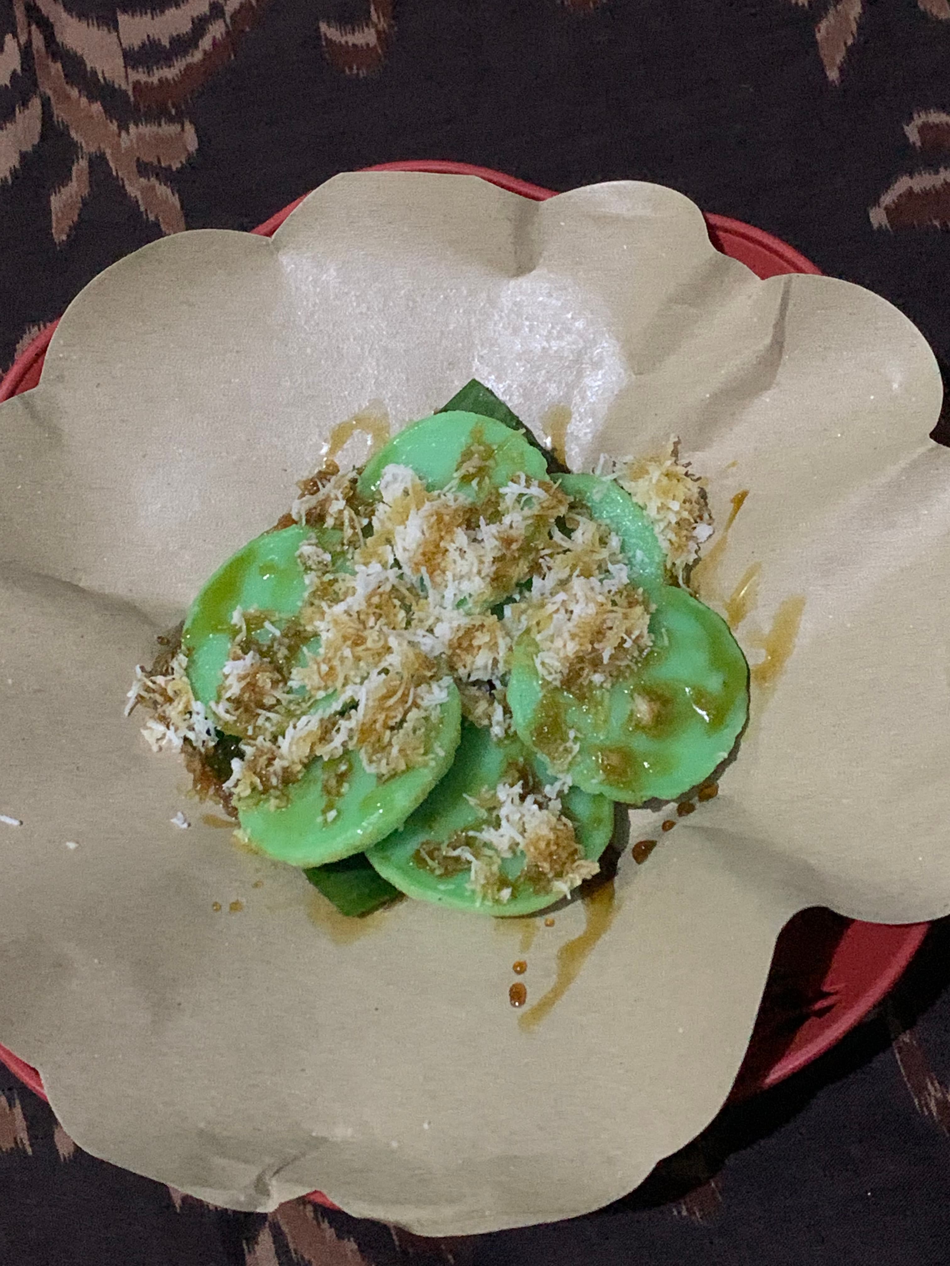 Kue Lak-Lak hijau berbentuk bundar dengan taburan kelapa parut dan siraman gula merah cair