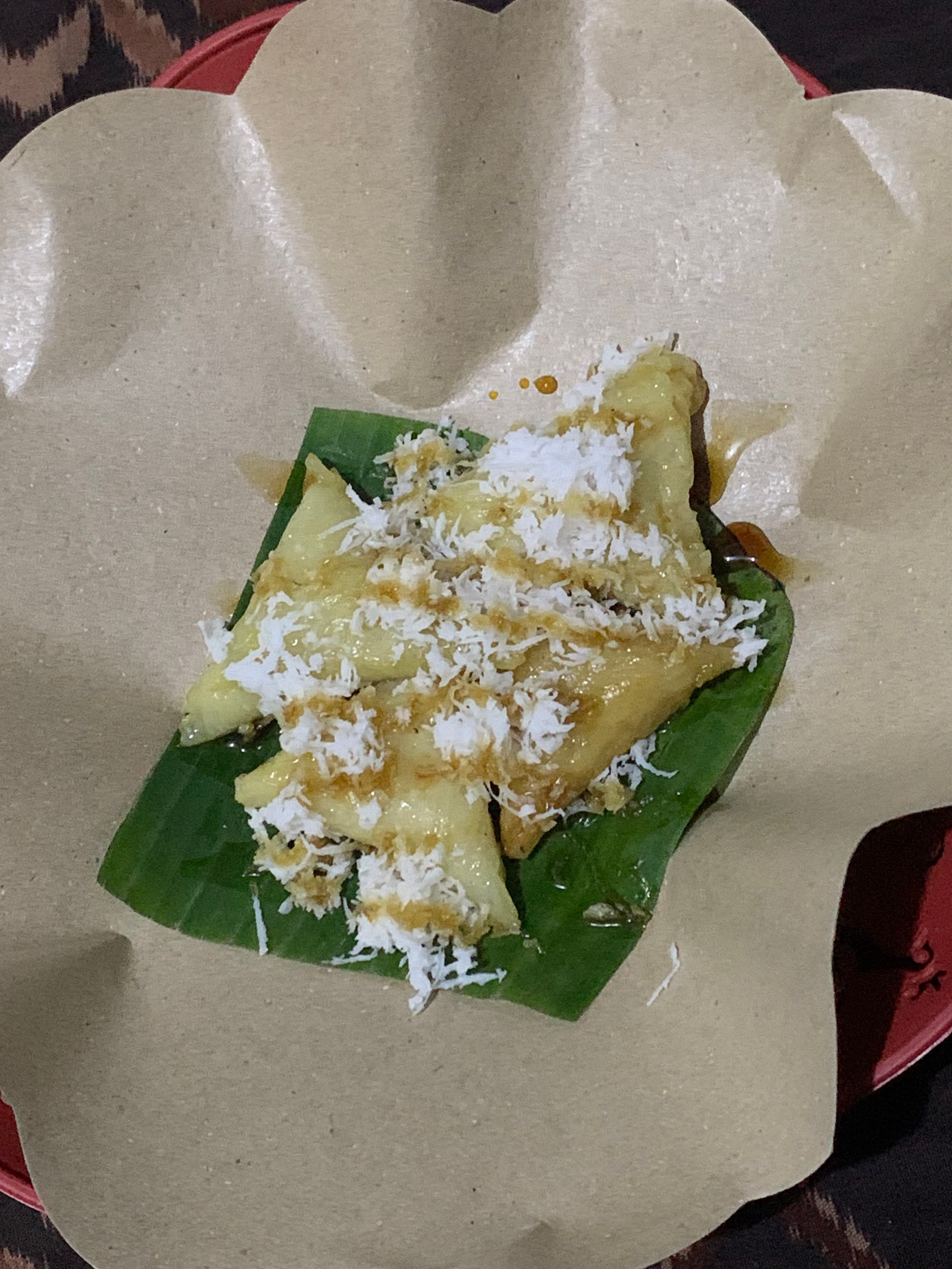 Kue Lukis di atas daun pisang dari jarak dekat, dengan taburan kelapa parut dan siraman gula merah yang merata