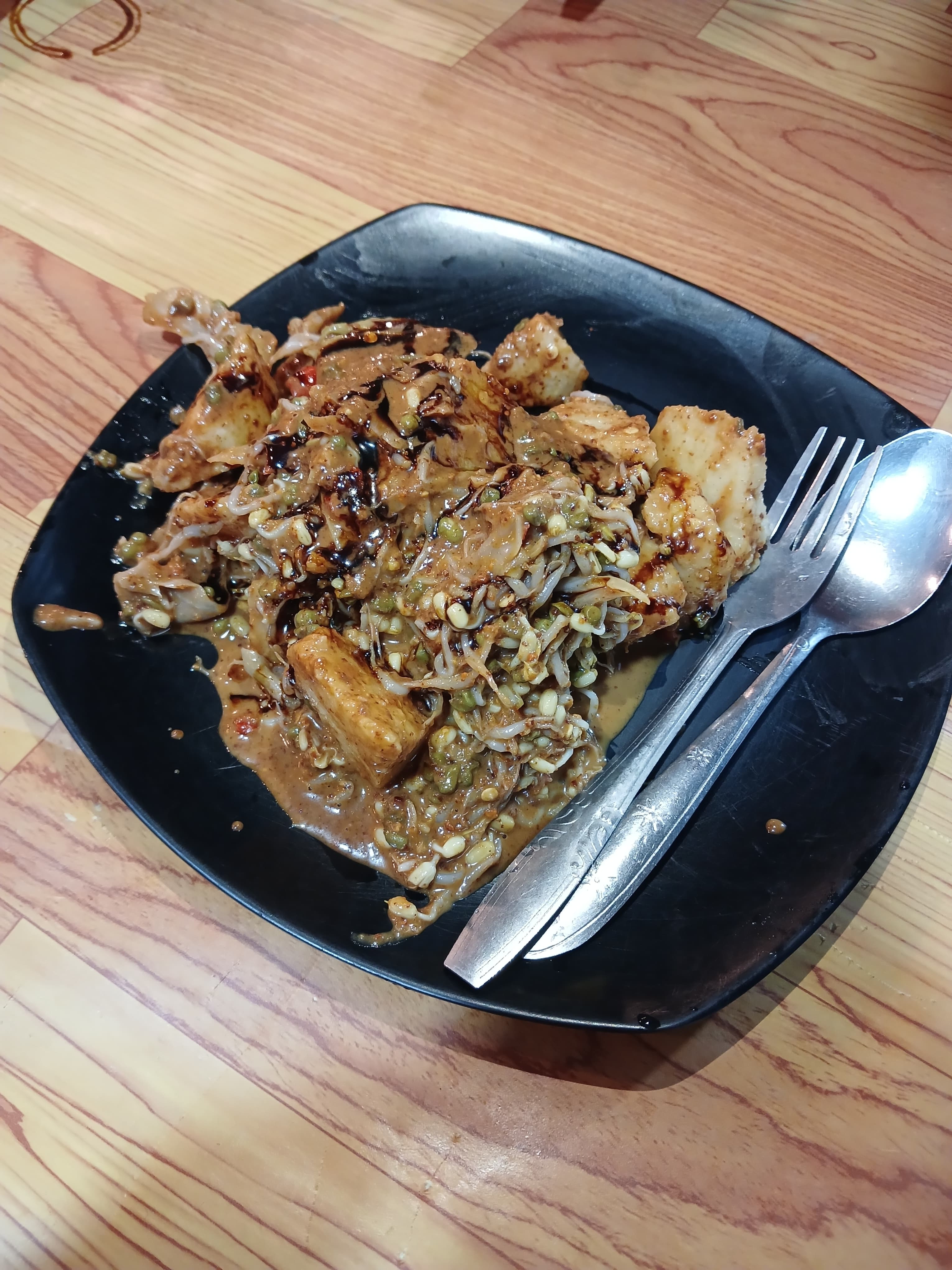 Tipat Cantok berupa ketupat dan tauge berbalut bumbu kacang gelap di atas piring hitam